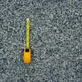 A yellow tape measure is laid vertically on a bed of gray gravel and crushed stone.