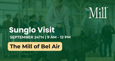 Promotional graphic for a Sunglo visit to The Mill of Bel Air, featuring a woman in a white shirt standing next to a dark pig in a barn-like setting, with large white text and a yellow date/time box over a green-tinted photo.