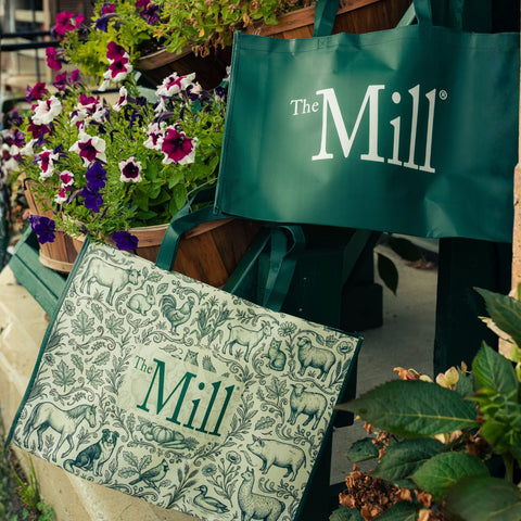 two mill branded tote bags hanging off of plants in a garden