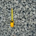 Gray gravel stones filling the frame with a yellow tape measure placed vertically to show size against the material.