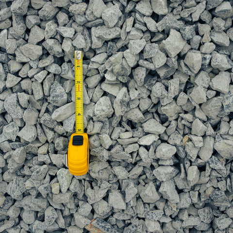 Gray gravel stones filling the frame with a yellow tape measure placed vertically to show size against the material.