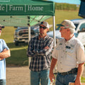 Three men standing under a green tent with 'Wildlife Farm Home' branding, in an outdoor setting.