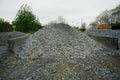 Heap of gravel with a cloudy sky and trees in the background