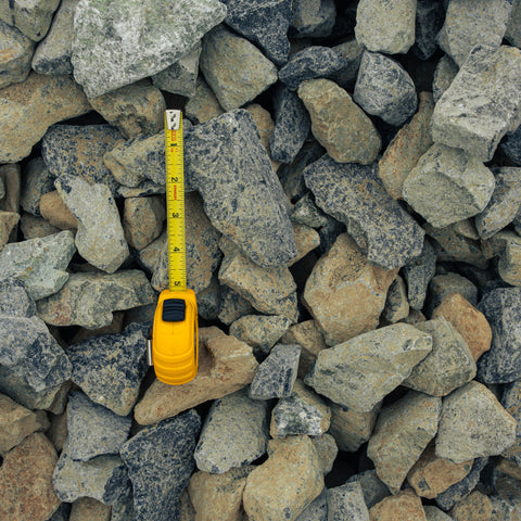 A yellow tape measure extended vertically among gray and beige stones to show size against a pile of rocks.
