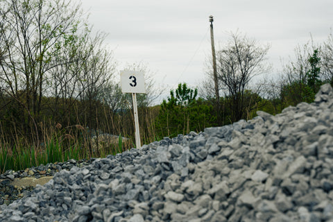 Gravel path with a sign indicating number 3, surrounded by trees and grass.