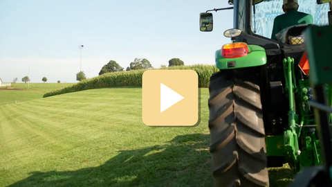 Green tractor on a grassy field with a play button overlay