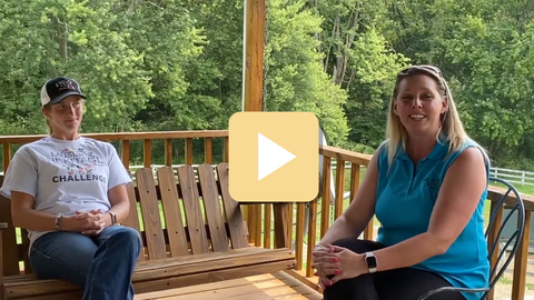 Two people sitting on a wooden bench outdoors with a play button overlay.