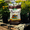 Bag of Espoma Organic Plant-tone plant food on a wooden table with gardening tools and plants in the background.
