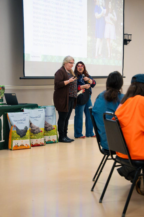 Two women presenting in front of an audience with a screen displaying an image in a room.