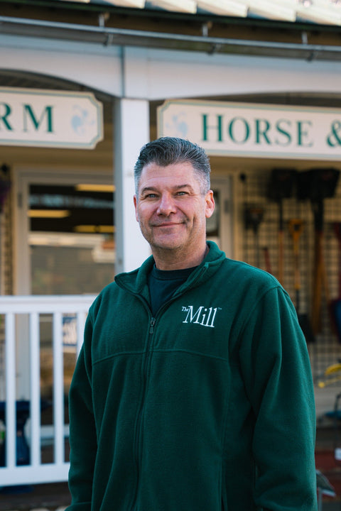 Man wearing a green jacket with a logo in front of a store named 'Horse & Mill'.