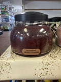 A Bourbon Berry Tavern Candle by A Cheerful Giver showing a lit candle in a glass jar with a berry and bourbon scent.