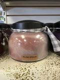 A Cheerful Giver Mama Island Breeze candle in a glass jar with a lit wick, surrounded by tropical decor and palm leaves.
