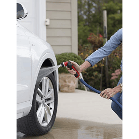 Person washing a white car with a hose and spray nozzle.