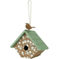 A decorative birdhouse with a green shingled roof, a wood-grain front panel decorated with white daisy patterns, a hanging loop, and a small brown bird figurine perched on top, shown against a plain white background.