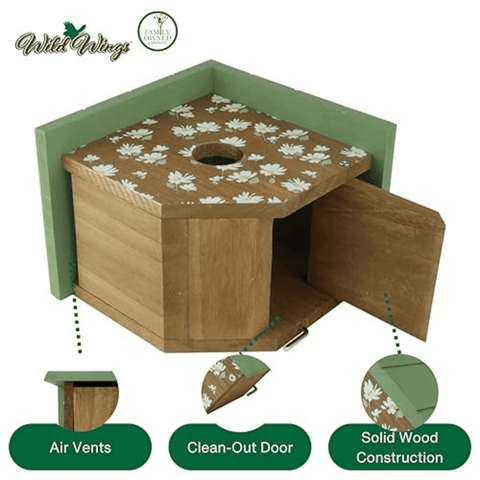 A wooden birdhouse with a green frame and lid, decorated with a white floral pattern on the top. The image includes feature callouts at the bottom highlighting air vents, a clean-out door, and solid wood construction, with the Wild Wings brand logo in the upper left.
