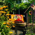 A bag of Peanut Blend Suet Balls placed on a wooden table in a garden setting, surrounded by yellow flowers, green foliage, and a small green birdhouse.