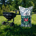 Fertilizer spreader and bag of Kentucky 31 seed on a grassy field with trees in the background