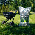 A grass seed spreader with a Mill Professional Grass Seed Bag next to it in a grassy yard