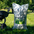 Bag of 'The Mill' professional seed mix on a grassy area with a lawn mower in the background.