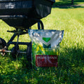 A grass seed spreader with The Mill Dense Shade grass seed bag resting against it in a grassy field