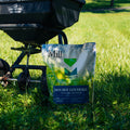 Black lawn spreader on grass with a bag of fertilizer labeled 'Mill' in the foreground.