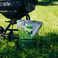 Lawn fertilizer spreader and bag on a grassy area with trees in the background