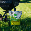 Black lawn spreader on grass with a bag of fertilizer labeled 'The Mill' in the foreground.
