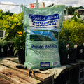 Bag of Coast of Maine Organic & Natural Raised Bed Mix on a wooden pallet with gardening tools and gloves.