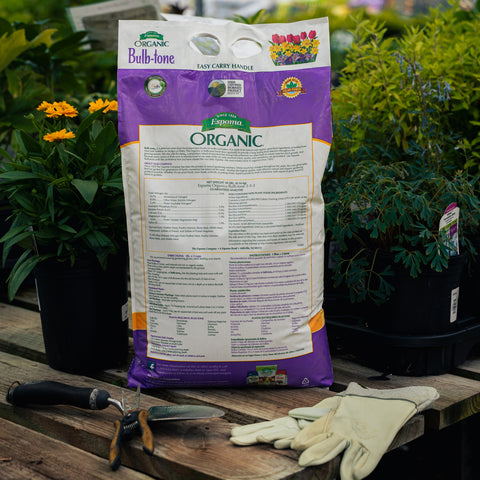 Bag of Organic Bulb-tone fertilizer on a wooden table with gardening tools and plants in the background.