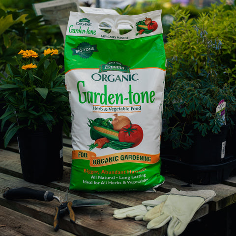 Bag of Espoma Organic Garden-tone fertilizer on a wooden table with gardening tools and gloves.