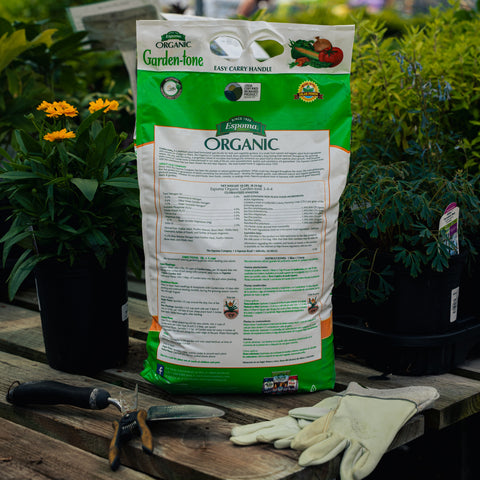 Bag of Garden-tone Organic fertilizer on a wooden table with gardening tools and gloves.