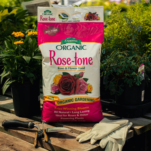 Bag of Organic Rose-tone Rose & Flower Food with gardening tools and gloves on a wooden surface.