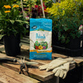 Polash fertilizer bag on a wooden table with gardening tools and gloves, surrounded by plants.