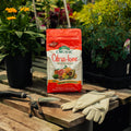 Bag of Organic Citrus-tone fertilizer on a wooden table with gardening tools and gloves, surrounded by plants.