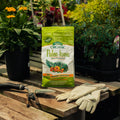 Bag of Palm-tone fertilizer on a wooden table with gardening tools and gloves, surrounded by plants.