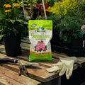 Bag of Organic Garden Lime with gardening gloves and tools on a wooden surface with plants in the background