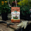 Bag of Espoma Organic Compost Starter on a wooden table with gardening tools and gloves, surrounded by plants.