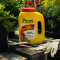 Yellow container of Preen Garden Weed Preventer with gardening gloves on a wooden surface.