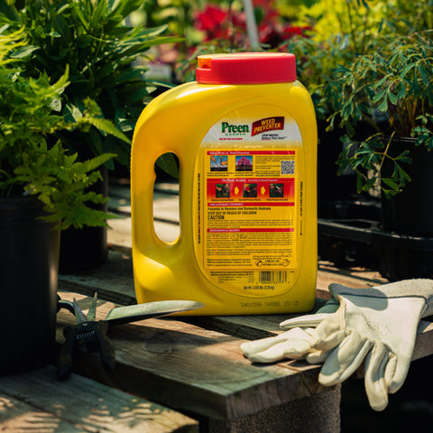Yellow garden fertilizer container with red lid on a wooden surface surrounded by plants