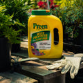 Yellow Preen garden weed preventer and plant food container on a wooden surface with gardening gloves.