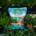A bag of Espoma Organic Seed Starter Premium Potting Mix standing upright in a garden setting with green plants around it.