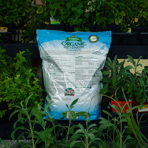 A bag of Espoma Organic Seed Starter fertilizer placed among green plants in a garden or nursery setting.