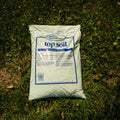 A bag of Jolly Gardener Top Soil placed on a patch of green grass outdoors.
