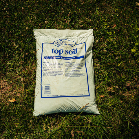 A bag of Jolly Gardener Top Soil placed on a patch of green grass outdoors.