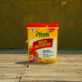 A yellow and red plastic bucket of Preen Garden Weed Preventer standing on a wooden deck in front of a yellow-green brick wall.