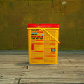 A yellow and red plastic bucket of Preen Garden Weed Preventer standing on a wooden deck in front of a yellow-green brick wall.
