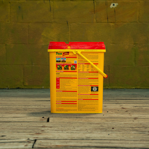 A yellow and red plastic bucket of Preen Garden Weed Preventer standing on a wooden deck in front of a yellow-green brick wall.