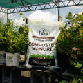 Bag of Twin Oaks Composted Manure with plants in the background