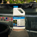 A white plastic jug of Cutrine Plus Aquatic herbicide with a blue cap, sitting on a stone pedestal in front of a black pond liner.