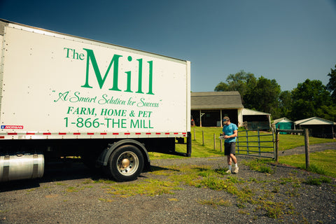 A white Mill delivery truck with a delivery driver standing next to it on a farm. 